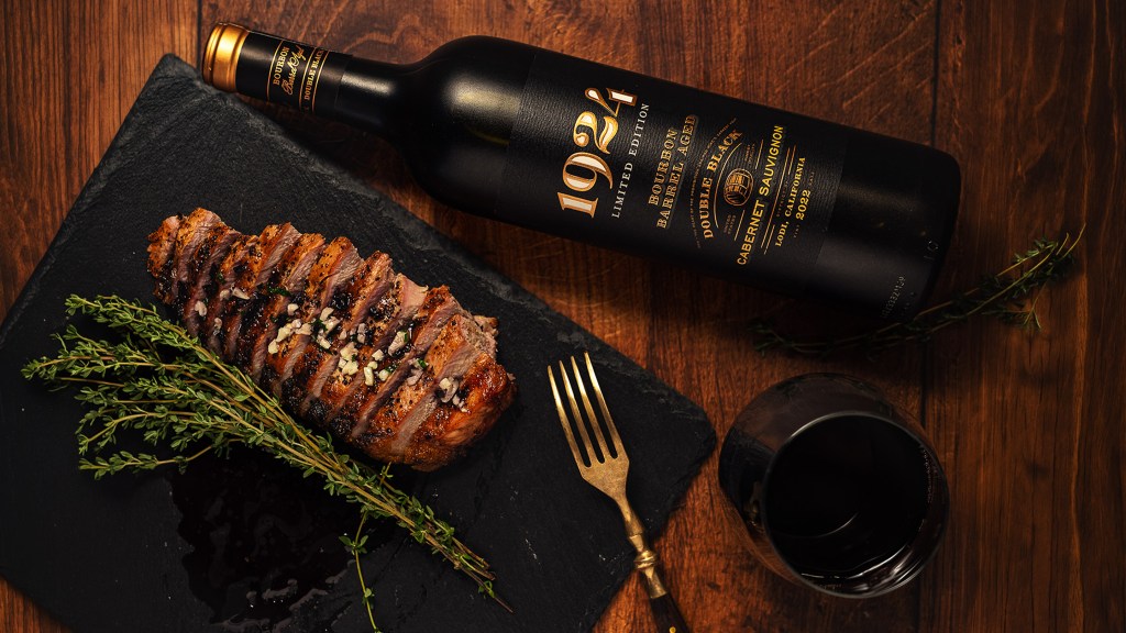 Photo of the 1924 Double Black Bourbon Barrel Cabernet Sauvignon with grilled bone-in pork chop on a black cutting board