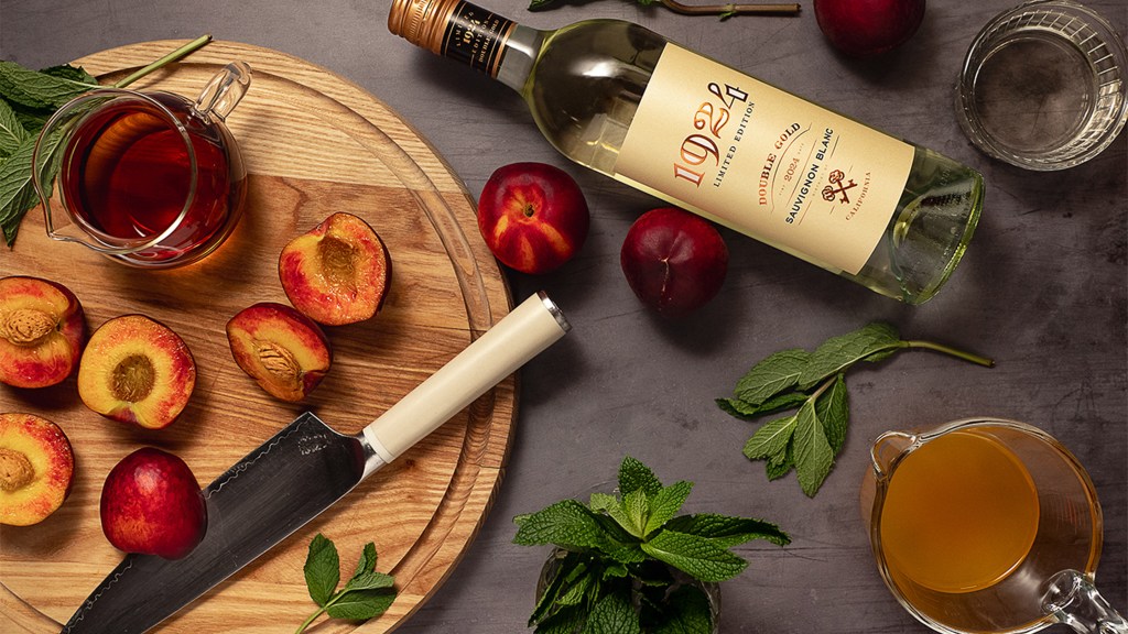 Photo of the 1924 Double Gold Sauvignon Blanc next to a cutting board with peaches and a glass of sangria