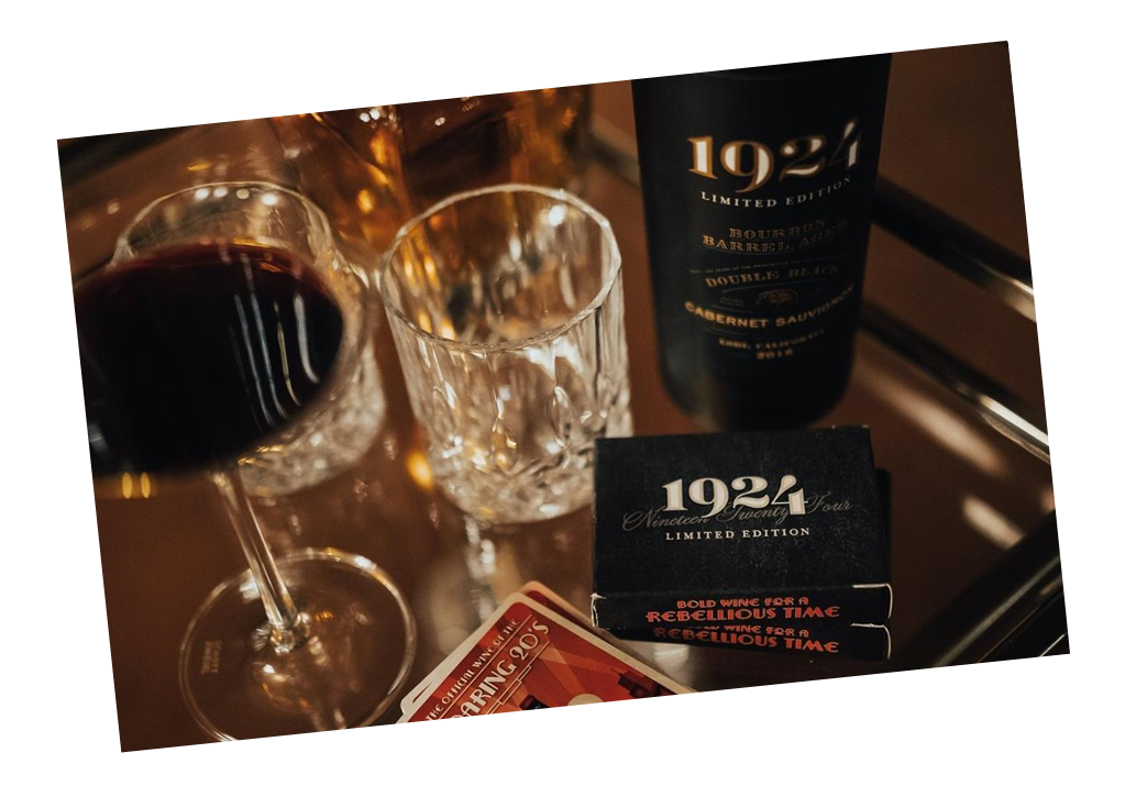 Speakeasy style photo with 1924 Cabernet Sauvignon and drinking glasses, playing cards, and a wine glass on a glass table.