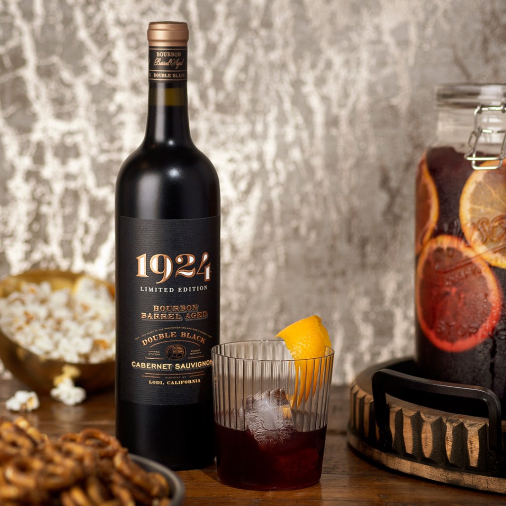Photo of the 1924 Barrel Aged Double Black Cabernet Sauvignon next to a cocktail glass and some pretzels