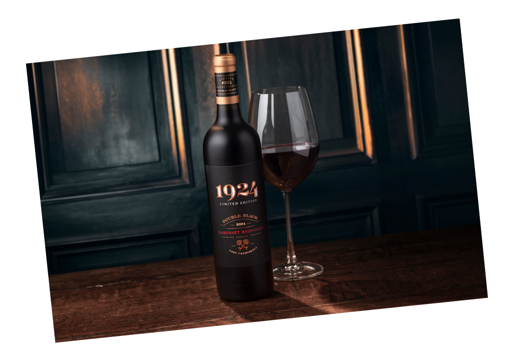 A dark moody image of 1924 Cabernet Sauvignon next to a wine glass on a wood counter